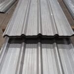 Tumpukan lembaran atap spandek galvalum profil trimdek untuk konstruksi bangunan industri.